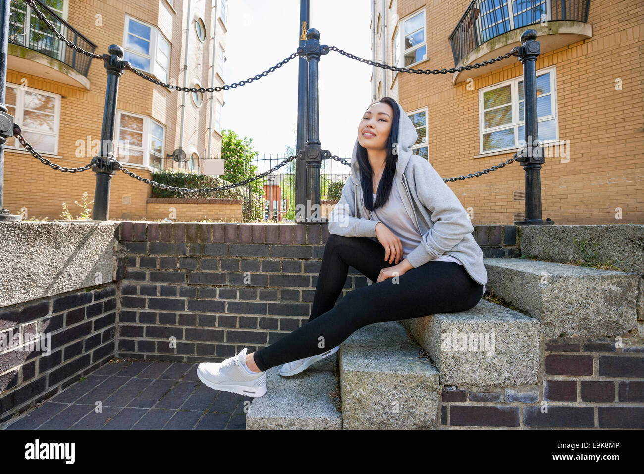 Full Length portrait of young woman sitting on stairs contre le bâtiment Banque D'Images