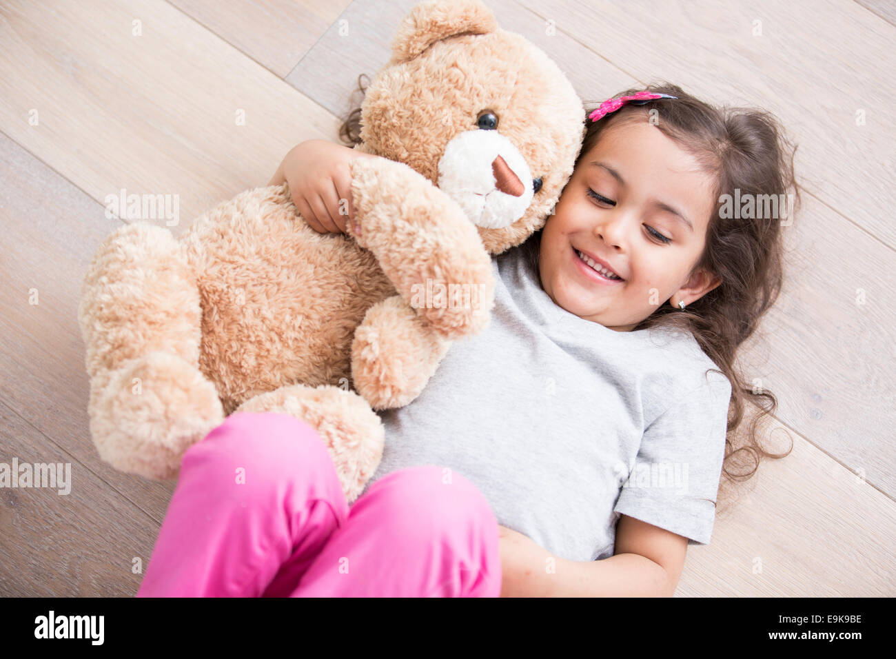 Fille avec ours couché sur un plancher en bois à la maison Banque D'Images