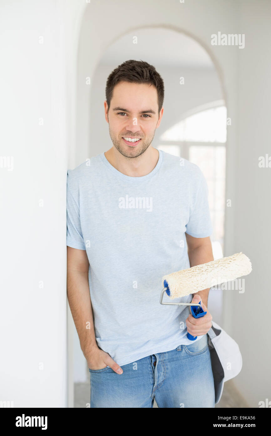 Portrait of handsome man holding paint roller in new house Banque D'Images
