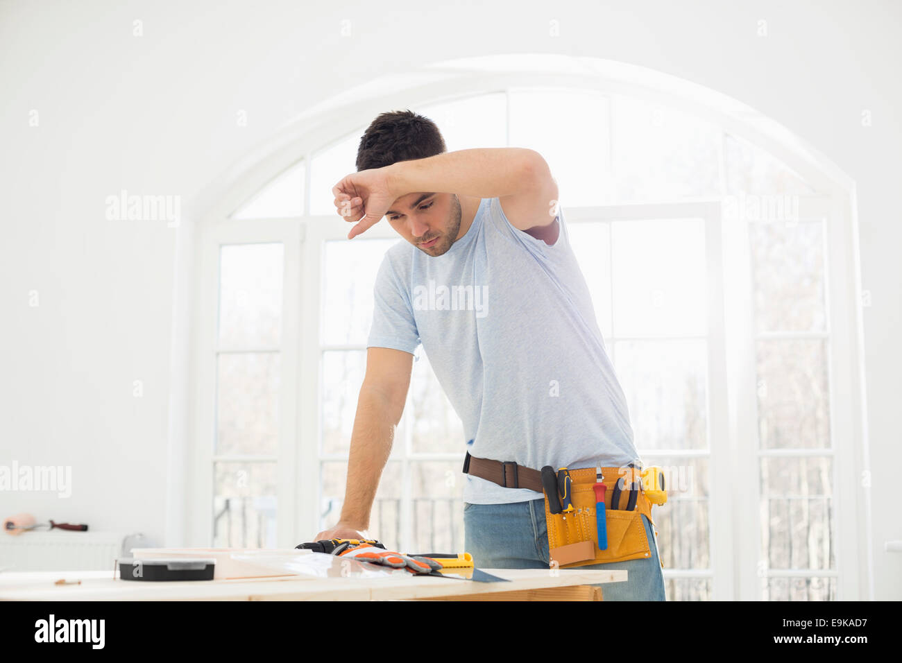 Mid-adult carpenter s'épongeant le front in new house Banque D'Images