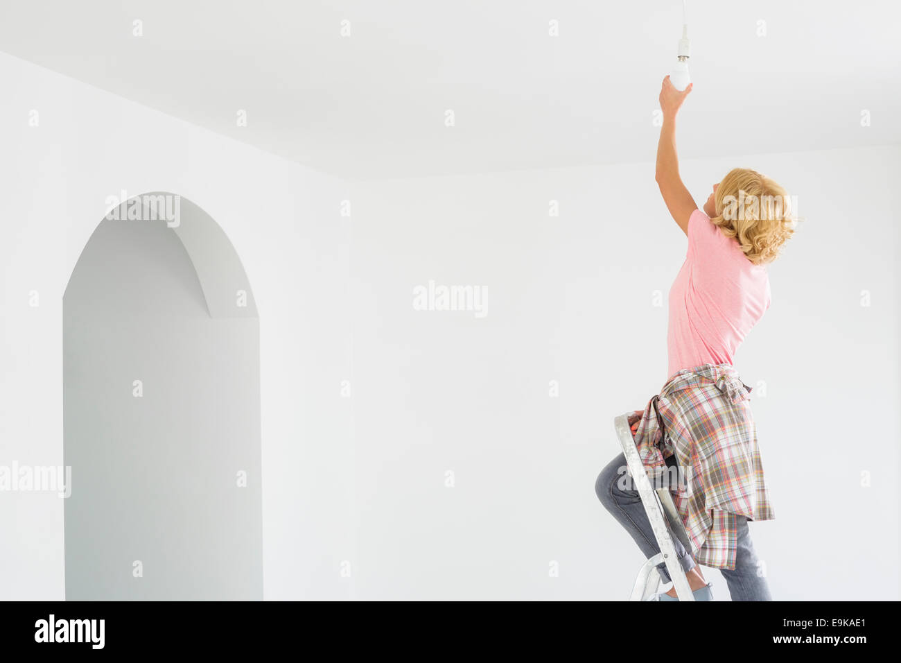 Femme sur l'échelle le montage ampoule dans nouvelle maison Banque D'Images