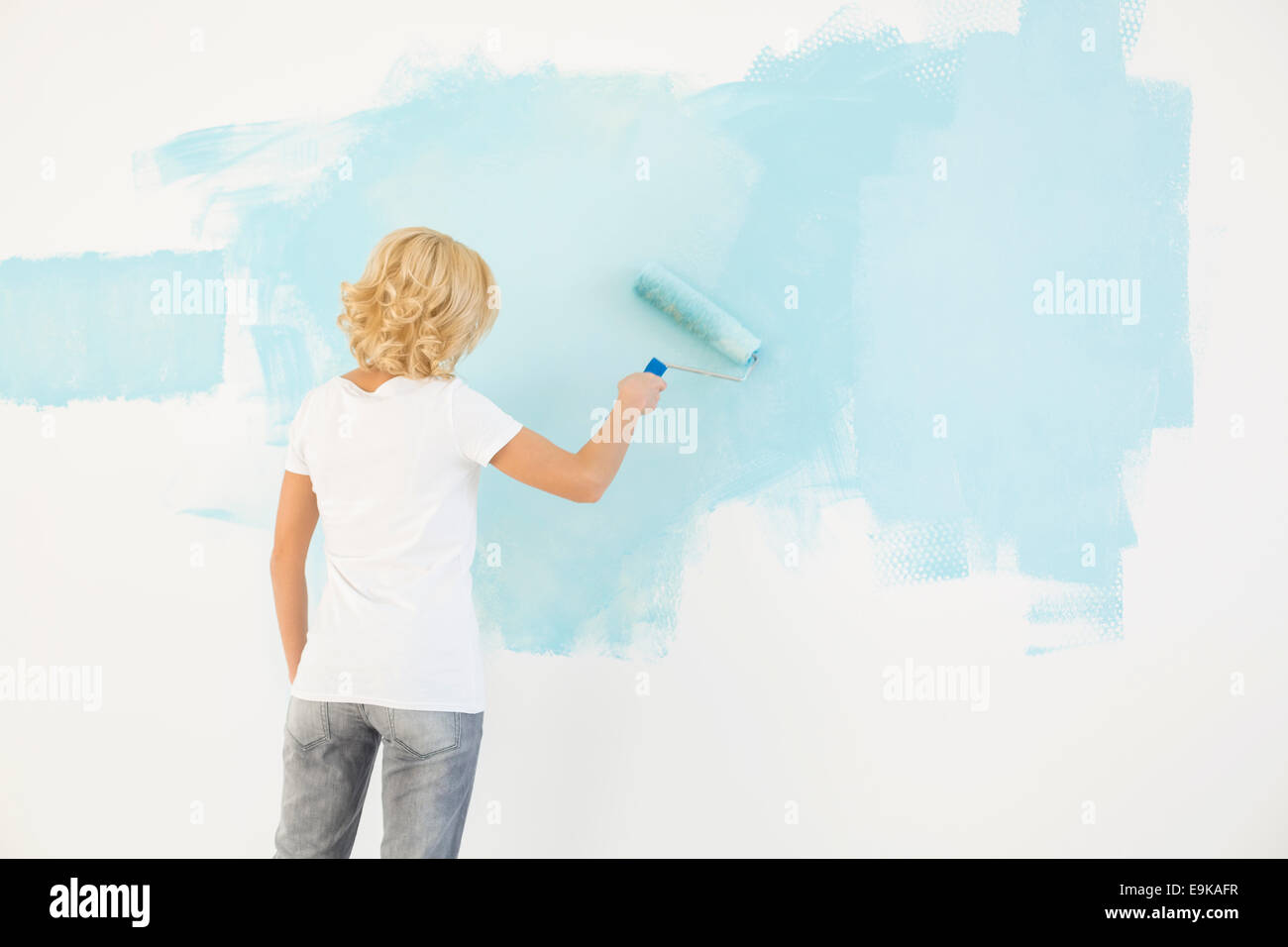 Rear view of woman painting wall with paint roller Banque D'Images
