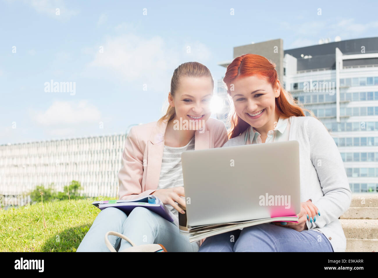 Smiling young university students using laptop avec bâtiments en arrière-plan Banque D'Images