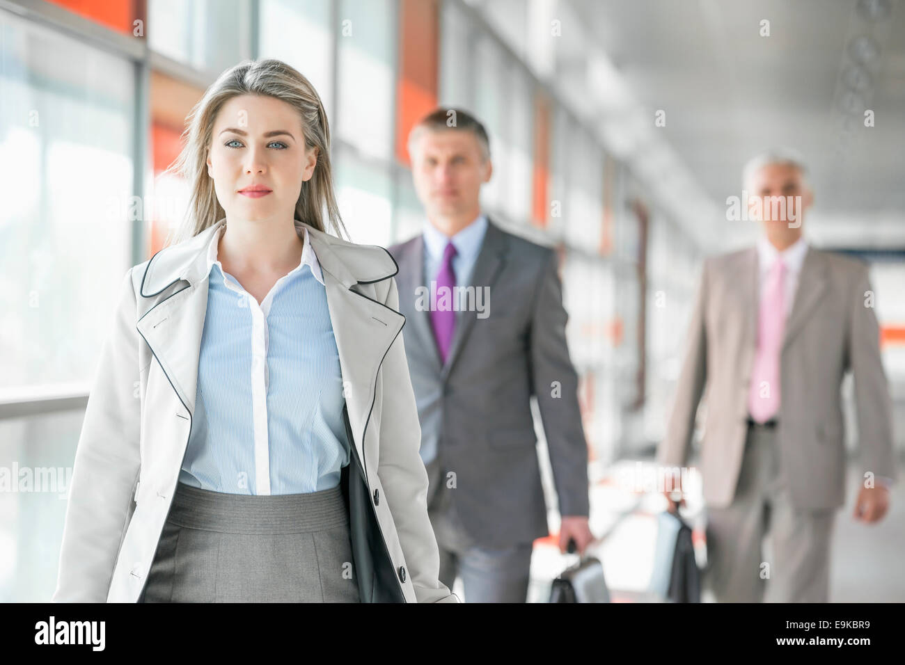 Belle jeune businesswoman walking avec des collègues masculins en arrière-plan à plate-forme du train Banque D'Images