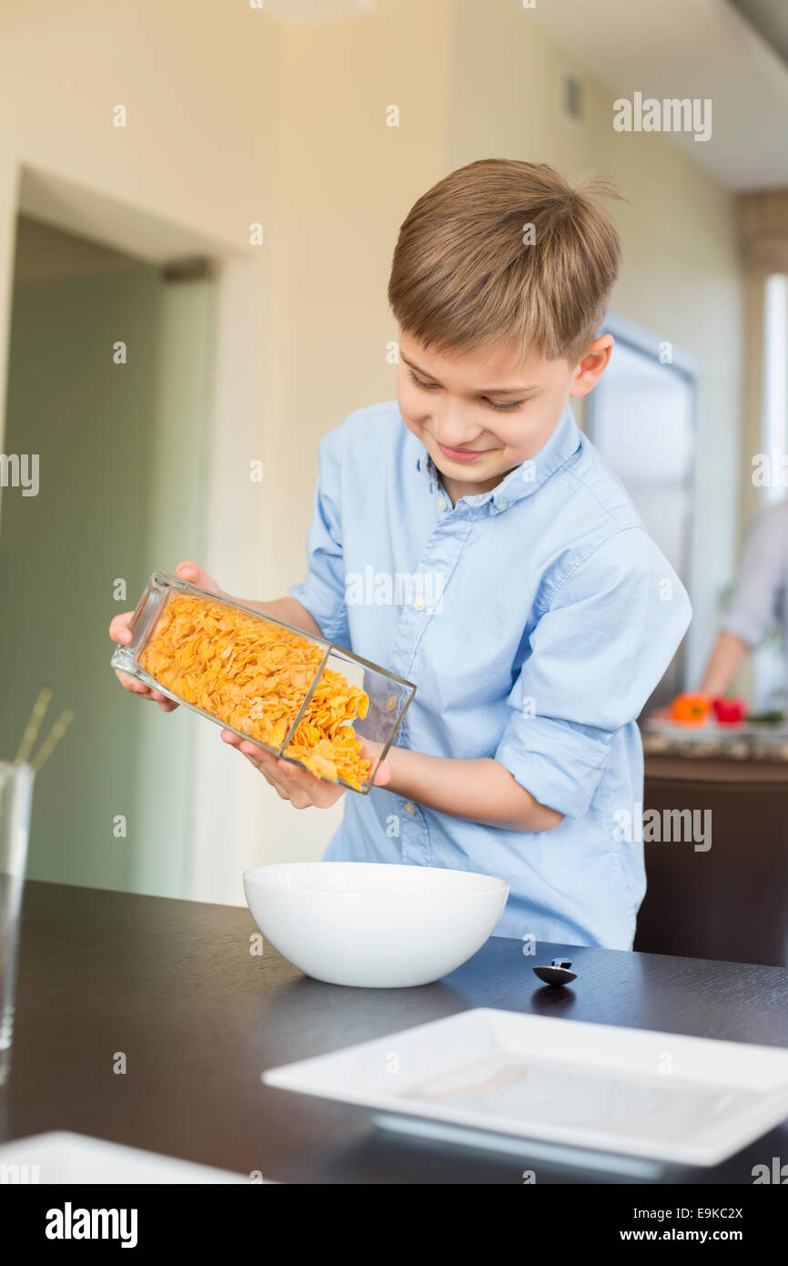 Smiling boy pouring flocons de maïs dans un bol à la maison Banque D'Images