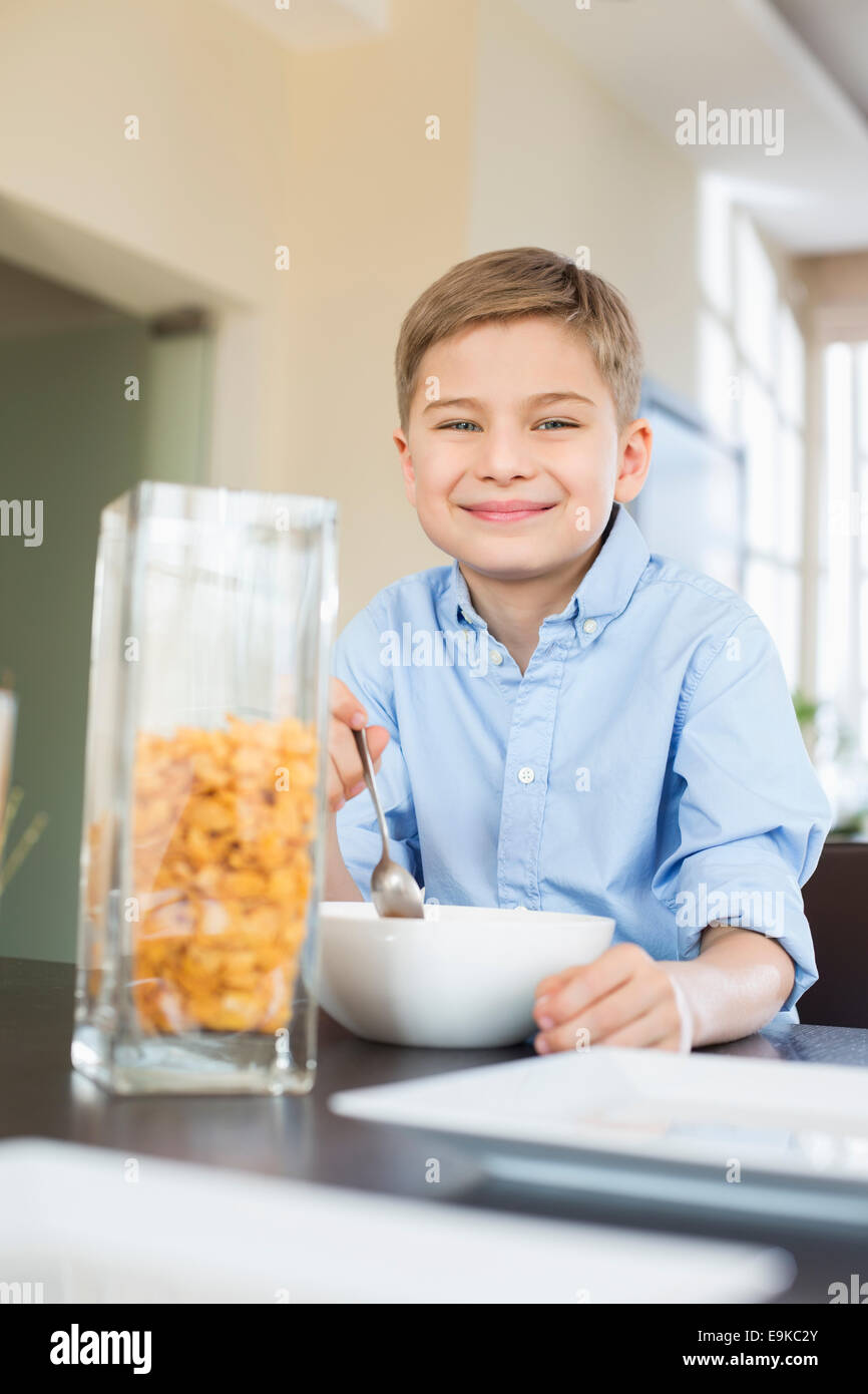 Portrait of smiling boy pouring flocons de maïs dans un bol à la maison Banque D'Images