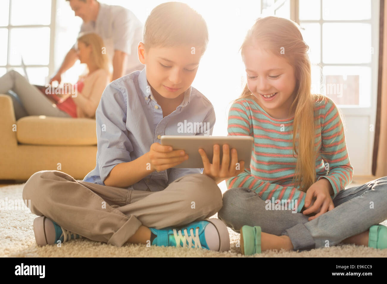 Frères et sœurs heureux using digital tablet sur le plancher avec les parents en arrière-plan Banque D'Images