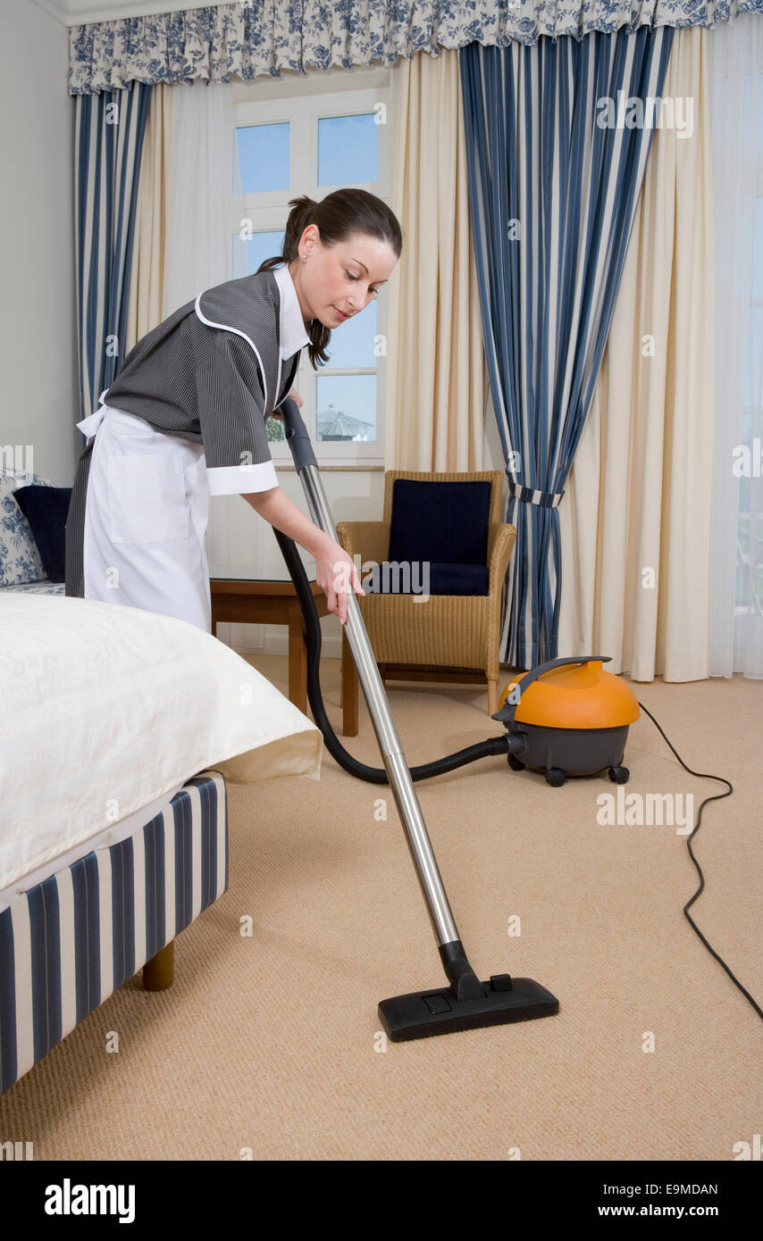 Femme de ménage en uniforme à l'aide d'aspirateur dans la chambre d'hôtel  Photo Stock - Alamy