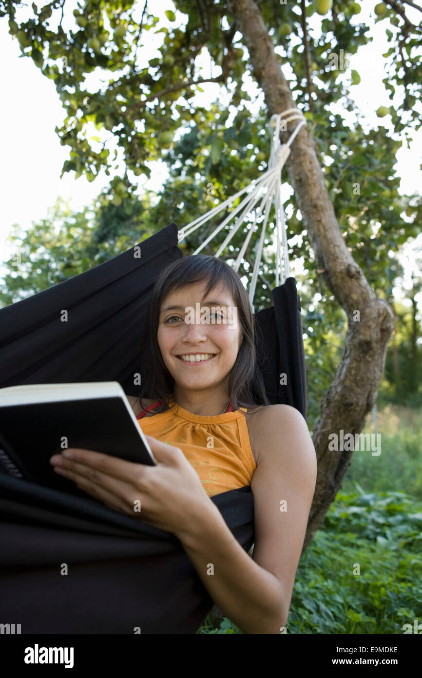 Young woman smiling and reading book in hammock Banque D'Images
