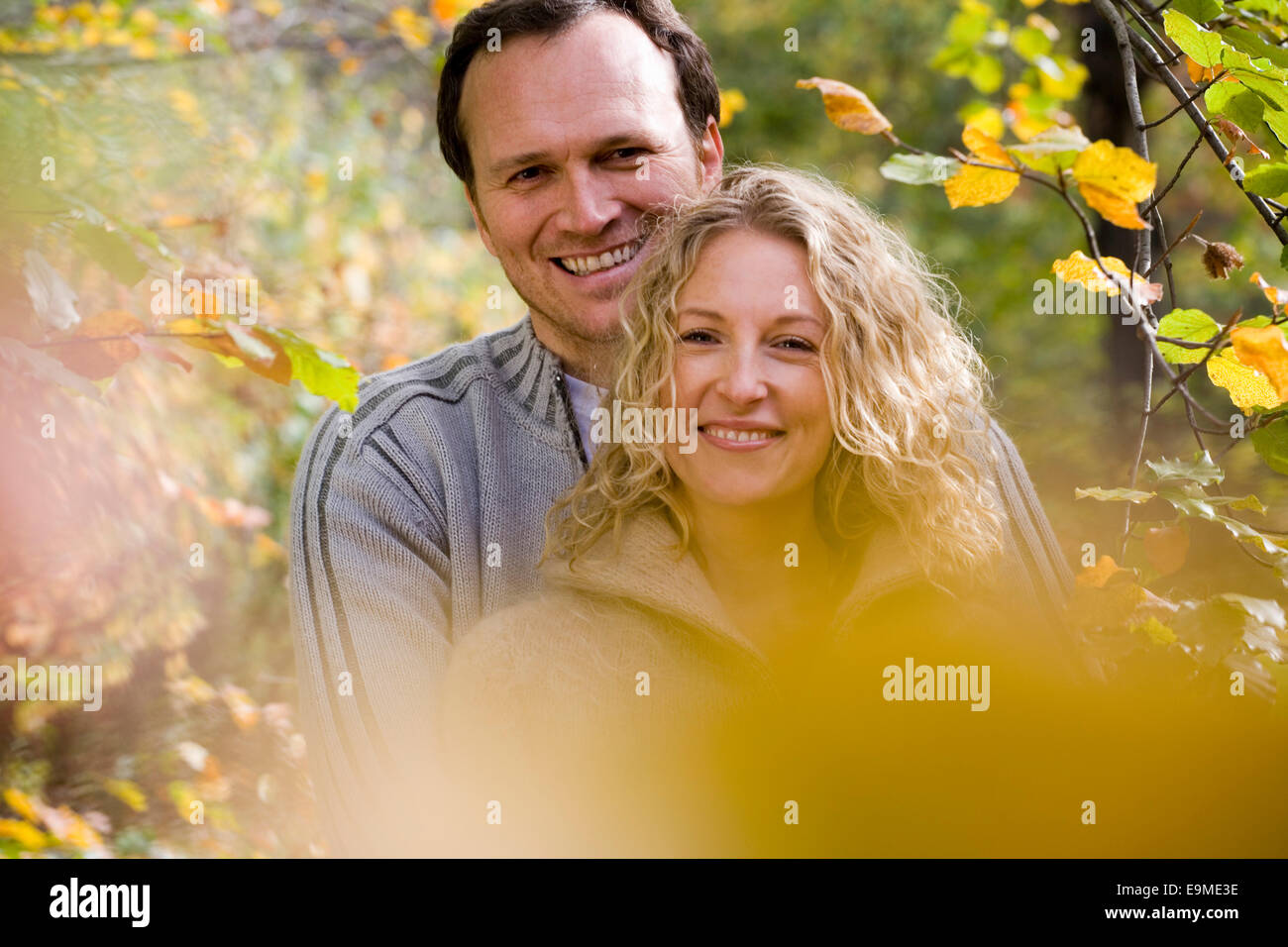 Young couple embracing entre les branches avec les feuilles d'automne Banque D'Images