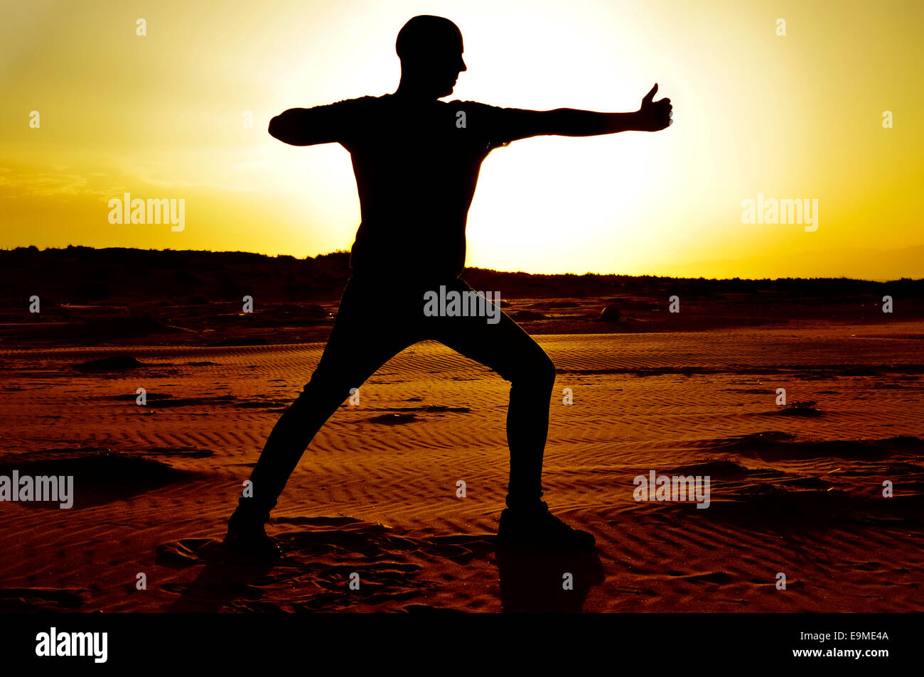 Un jeune homme pratiquant le yoga archer de poser dans les rétro-éclairage au coucher du soleil Banque D'Images
