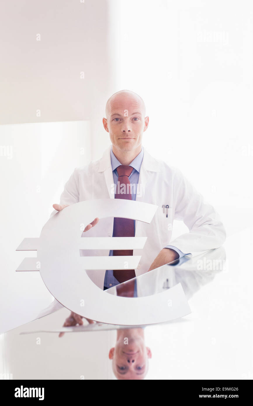 Portrait of male doctor holding symbole de l'euro à 24 en clinique Banque D'Images