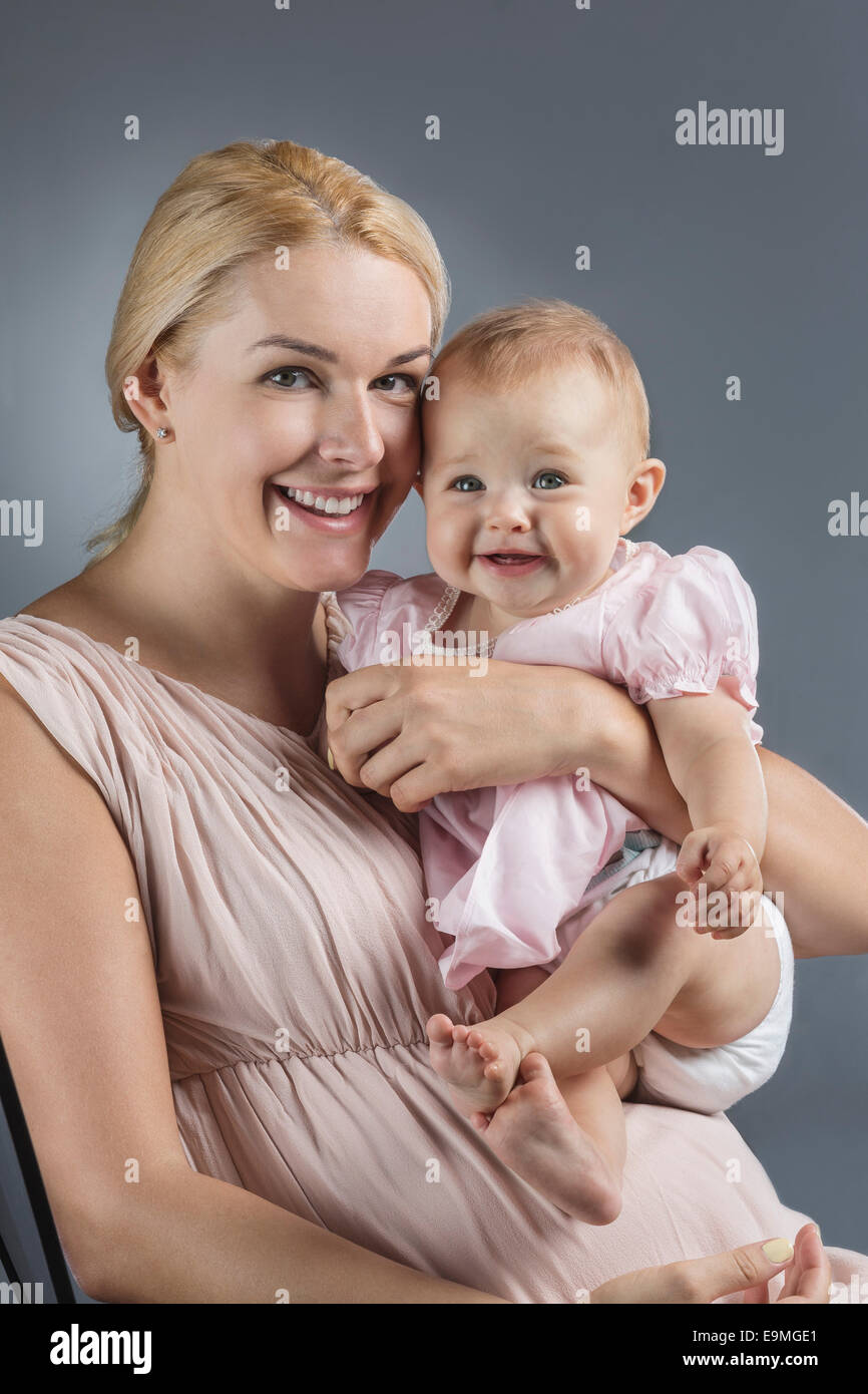 Portrait of happy mother carrying cute baby girl contre l'arrière-plan gris Banque D'Images