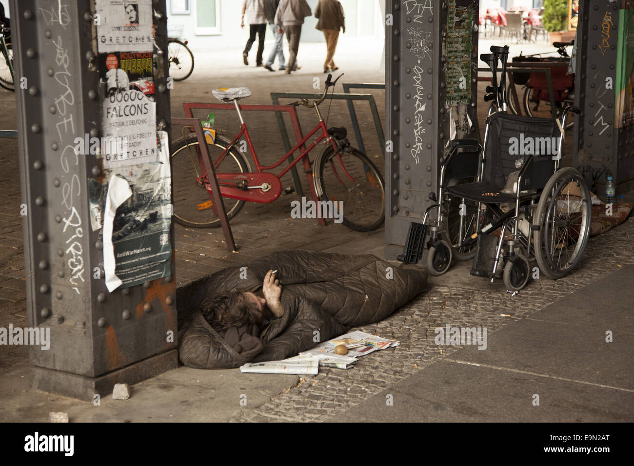 Mobilité sans-abri en appui sous un pont ferroviaire avec son fauteuil roulant à proximité. Berlin, Allemagne Banque D'Images