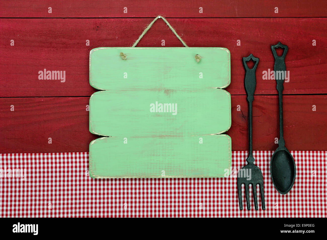 Vert blanc en bois rustique en fonte signe par cuillère et fourchette et nappe à carreaux rouge accroché sur un mur en bois rouge Banque D'Images