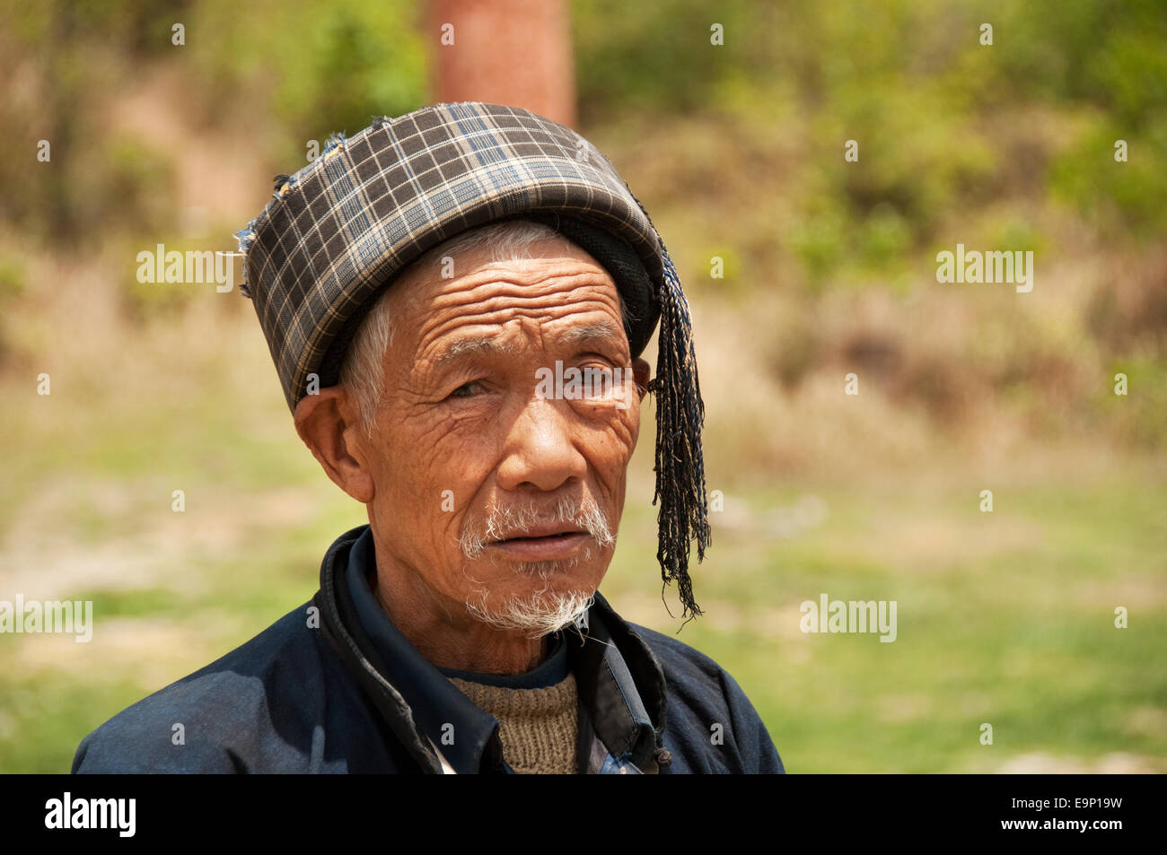 Portrait en gros plan d'un homme âgé de Buyei (Bouyei) portant un chapeau à carreaux à pampilles, province du Guizhou, Chine Banque D'Images