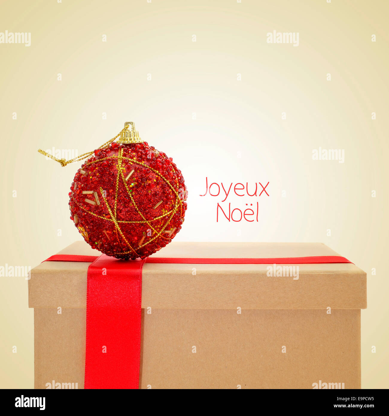 Un cadeau avec un ruban rouge et une boule de noël, et la phrase joyeux Noel, joyeux Noël en français, sur un fond beige, w Banque D'Images