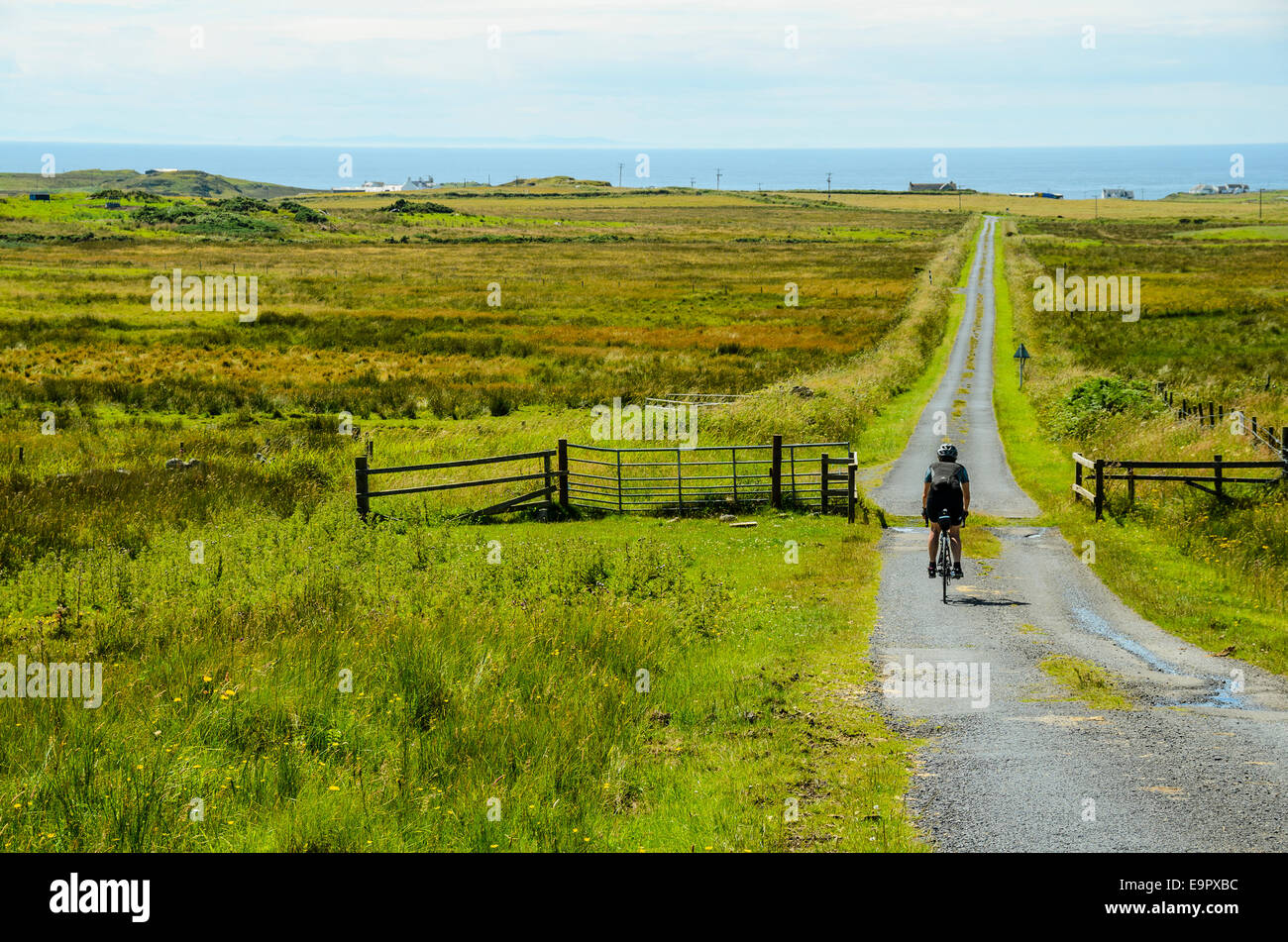 Cycliste féminine sur route vide sur le Rhinns d'Islay, l'île d'Islay, l'Écosse, avec l'Irlande du Nord à distance Banque D'Images