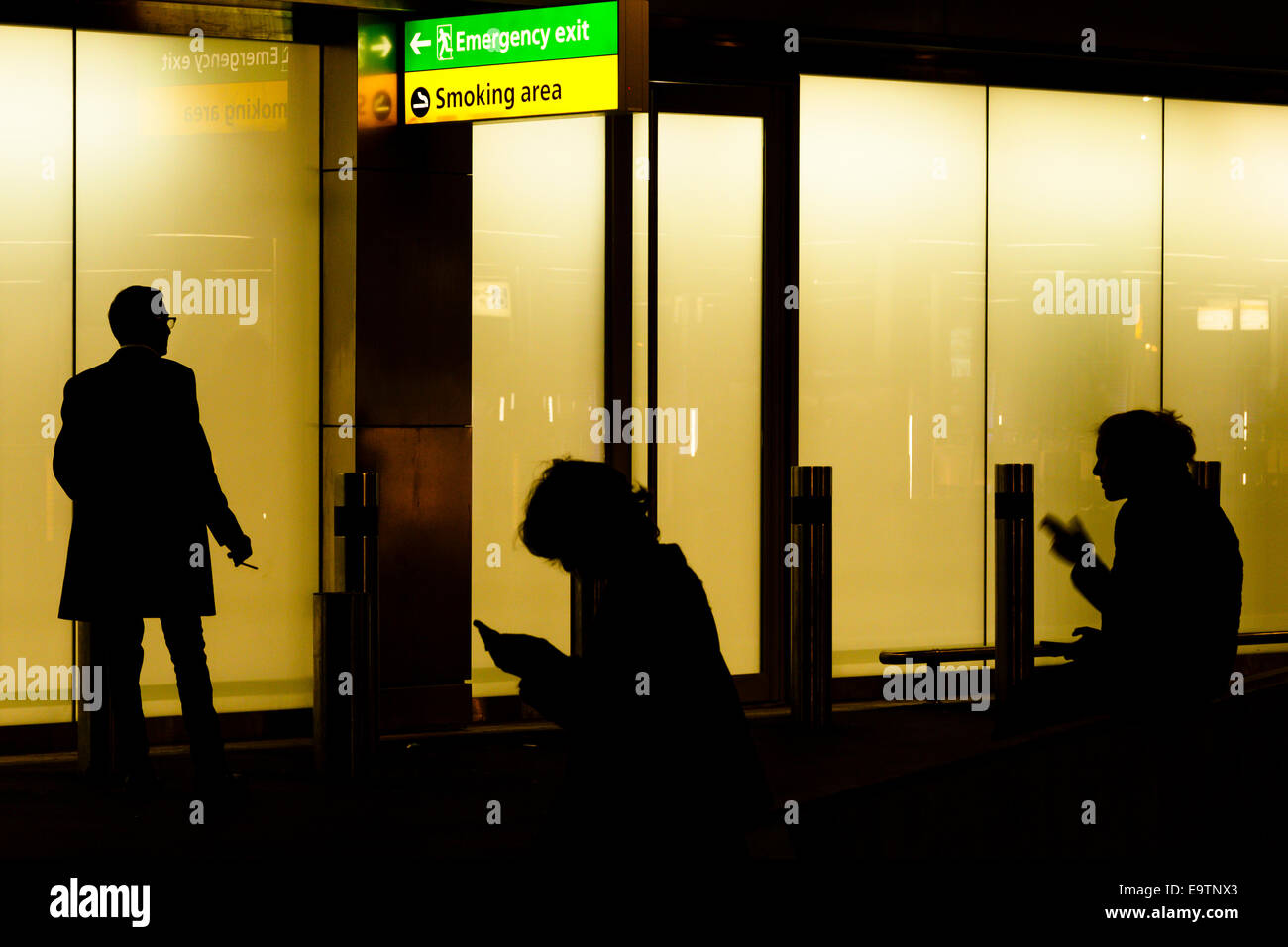 Trois fumeurs dans les fumeurs à l'extérieur du bâtiment la nuit. Banque D'Images