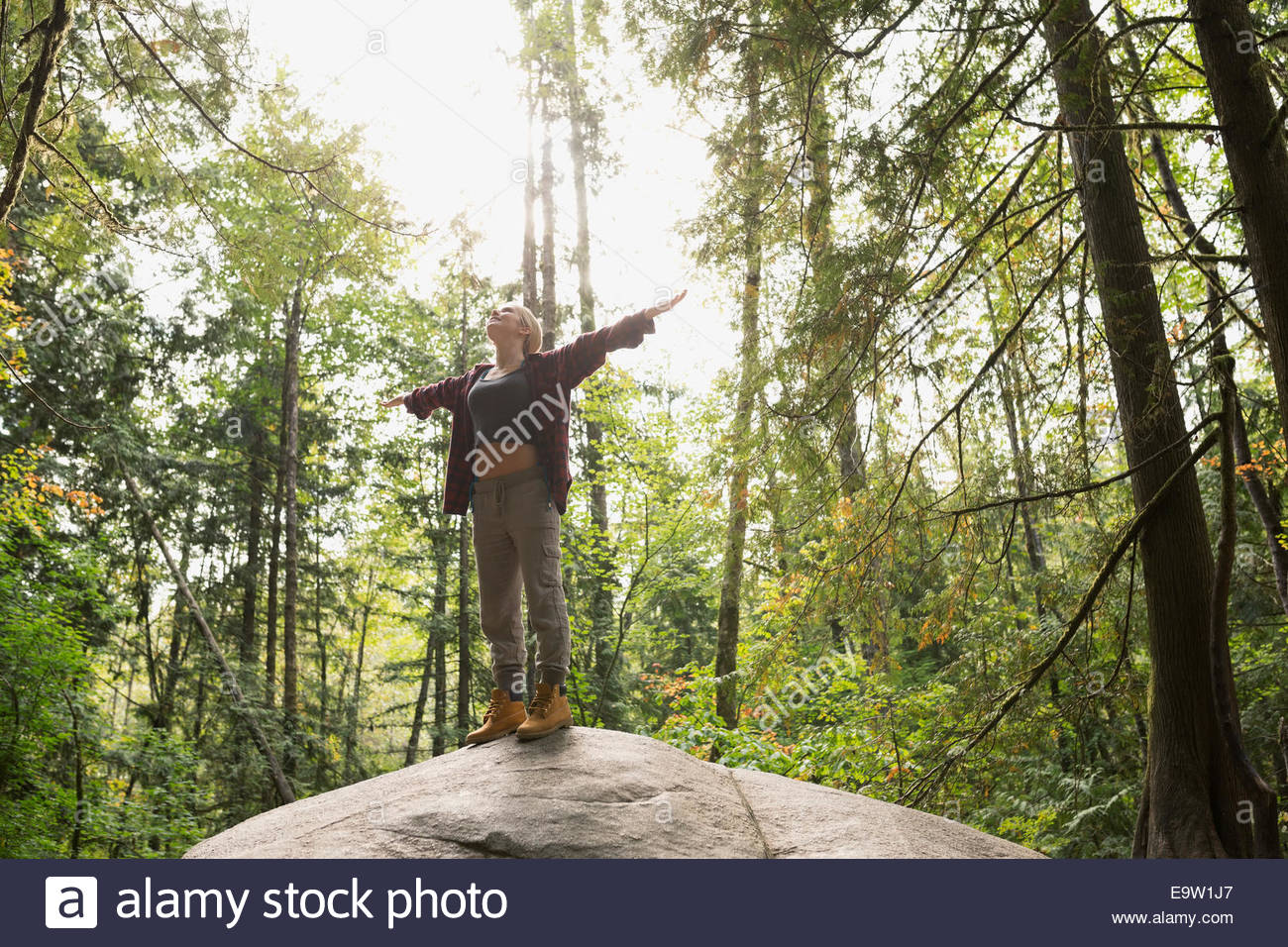 Woman with arms outstretched on rock in woods Banque D'Images