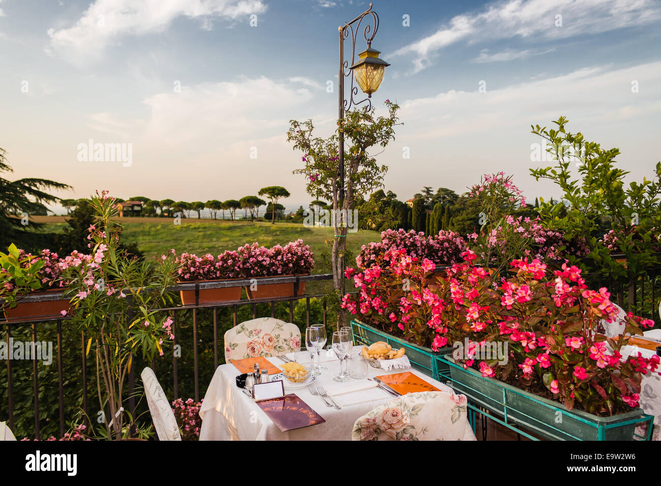 Tables de dîner dans l'élégant restaurant italien de style outdoor sur caillebotis fer parapet sur les collines de Dozza (Bo) en Italie dans une journée ensoleillée d'été : du vrai rouge, jaune et fleurs roses avec des feuilles vertes en pots vert tout autour. Serviettes de table Nappe rose et chic, Banque D'Images Tables de dîner dans l'élégant restaurant italien de style outdoor sur caillebotis fer parapet sur les collines de Dozza (Bo) en Italie dans une journée ensoleillée d'été : du vrai rouge, jaune et fleurs roses avec des feuilles vertes en pots vert tout autour. Serviettes de table Nappe rose et chic, Banque D'Images