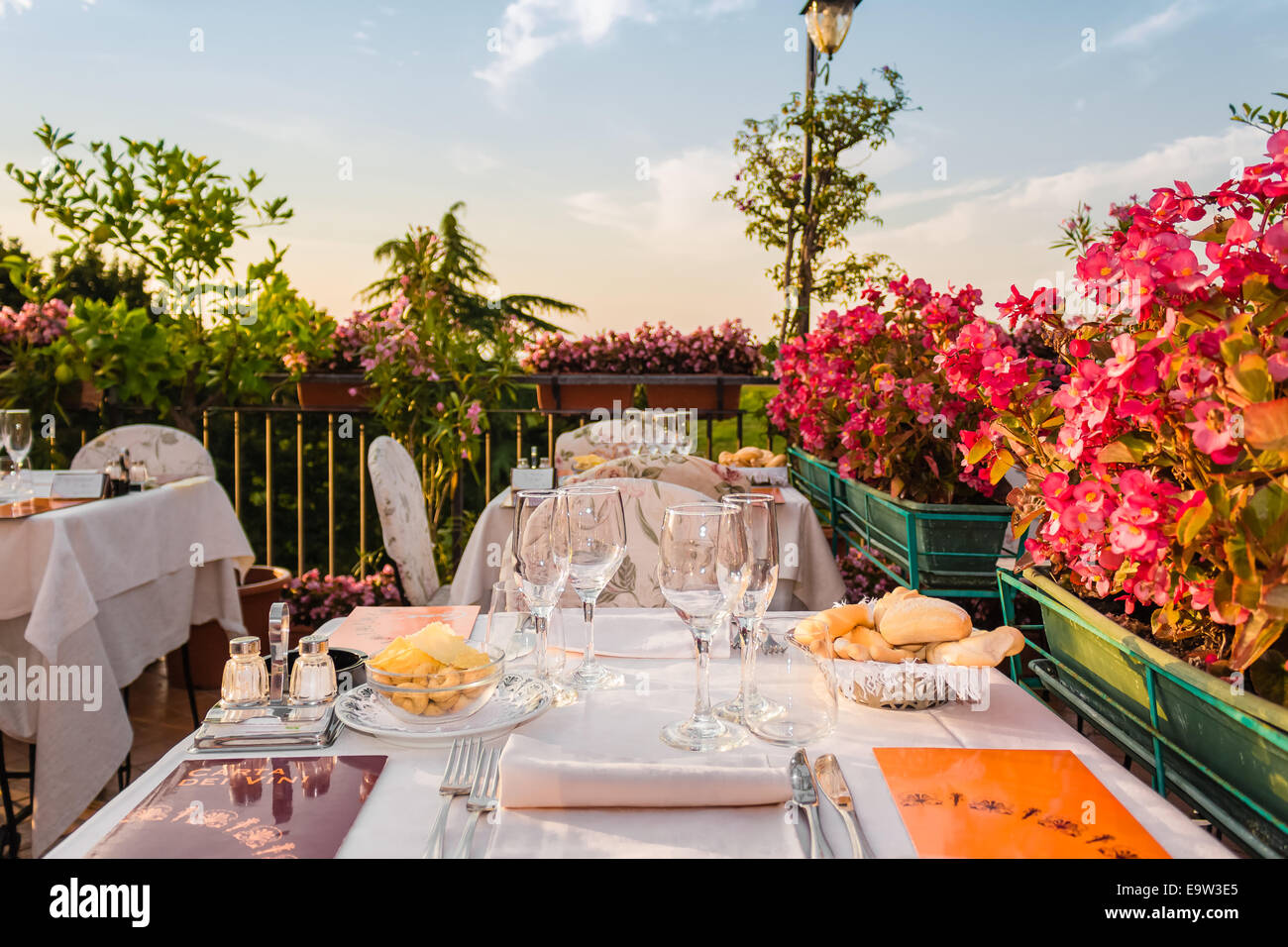 Tables de dîner dans l'élégant restaurant italien de style outdoor sur caillebotis fer parapet sur les collines de Dozza (Bo) en Italie dans une journée ensoleillée d'été : du vrai rouge, jaune et fleurs roses avec des feuilles vertes en pots vert tout autour. Serviettes de table Nappe rose et chic, Banque D'Images Tables de dîner dans l'élégant restaurant italien de style outdoor sur caillebotis fer parapet sur les collines de Dozza (Bo) en Italie dans une journée ensoleillée d'été : du vrai rouge, jaune et fleurs roses avec des feuilles vertes en pots vert tout autour. Serviettes de table Nappe rose et chic, Banque D'Images