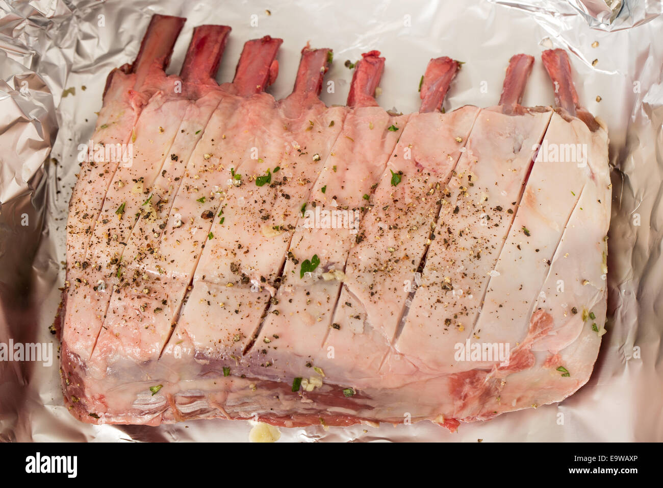 Un carré d'agneau cru frottée avec du sel, poivre, Herbes et Ail, sur une feuille d'aluminium avant d'être torréfiés. Banque D'Images