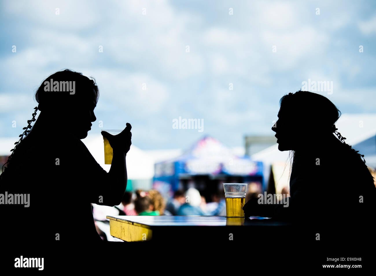 Deux jeunes filles en silhouette femme assis à parler de boire des pintes de bière blonde au cidre de la lumière au cinéma 2014 Banque D'Images