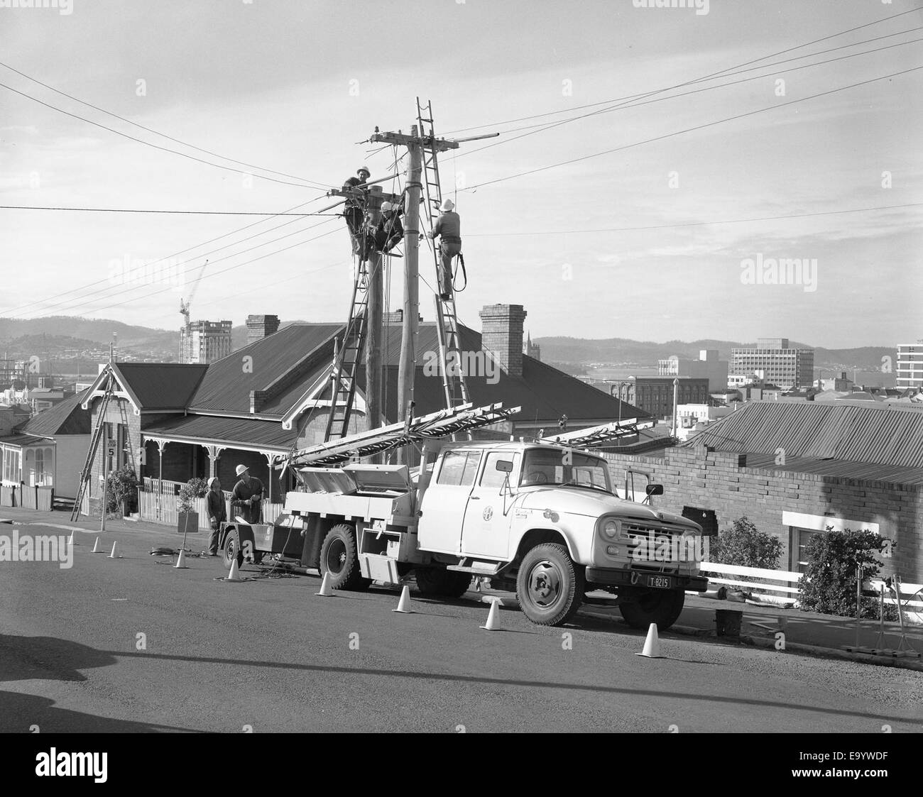 Cette photographie montre des hommes de ligne de la Commission Hydro Electric (H.E.C.) au travail, qui maintiennent les services électriques à l'intersection des rues Bathurst et Barrack en 1969, soulignant le travail essentiel dans le développement de l'infrastructure électrique de Tasmanie. Banque D'Images Cette photographie montre des hommes de ligne de la Commission Hydro Electric (H.E.C.) au travail, qui maintiennent les services électriques à l'intersection des rues Bathurst et Barrack en 1969, soulignant le travail essentiel dans le développement de l'infrastructure électrique de Tasmanie. Banque D'Images