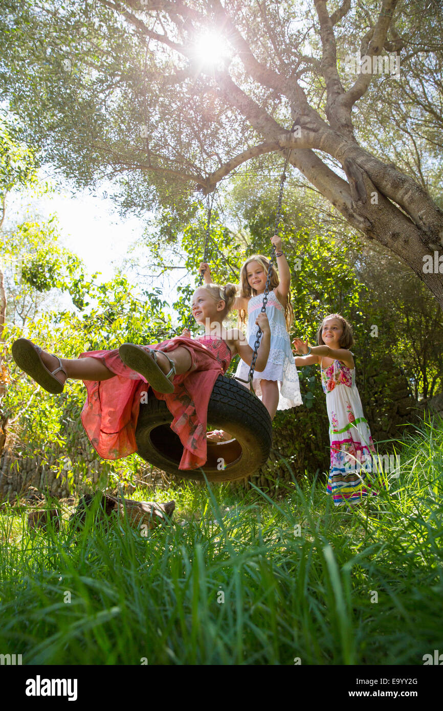 Portrait de trois jeunes filles, jouant sur l'arbre balançoire pneu dans jardin Banque D'Images