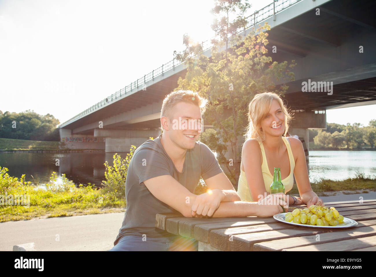 Jeune couple en train de boire une bière sur le banc de pique-nique au bord de la rivière Banque D'Images