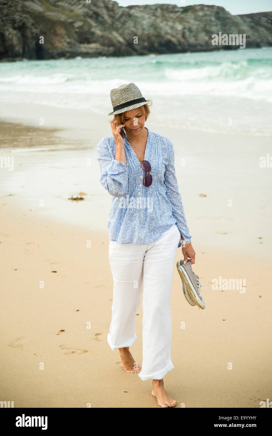 Young woman chatting on smartphone tout en flânant sur la plage, à Camaret-sur-mer, Bretagne, France Banque D'Images