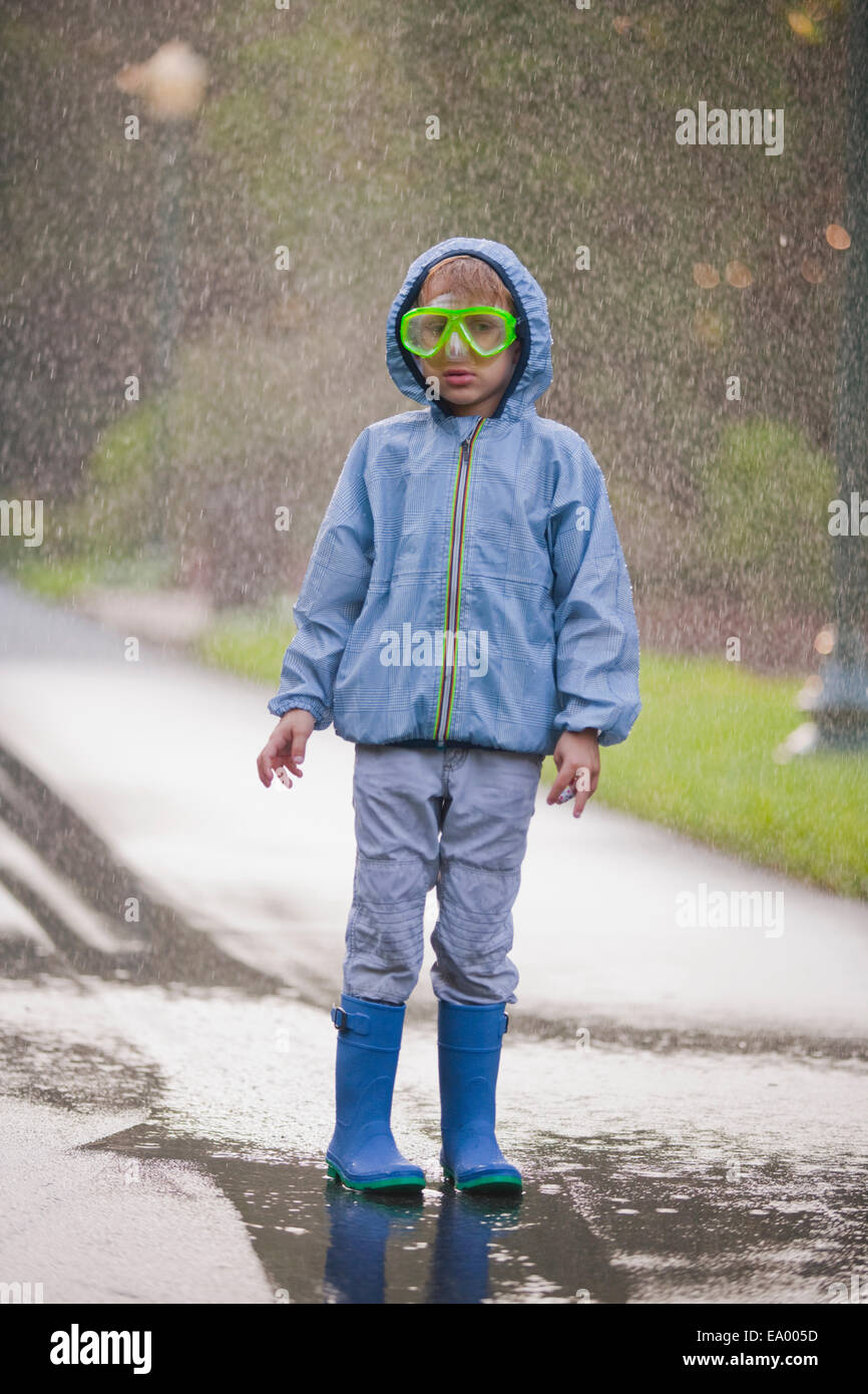 Portrait de jeune garçon portant des lunettes de plongée et des bottes en caoutchouc standing in street flaque Banque D'Images