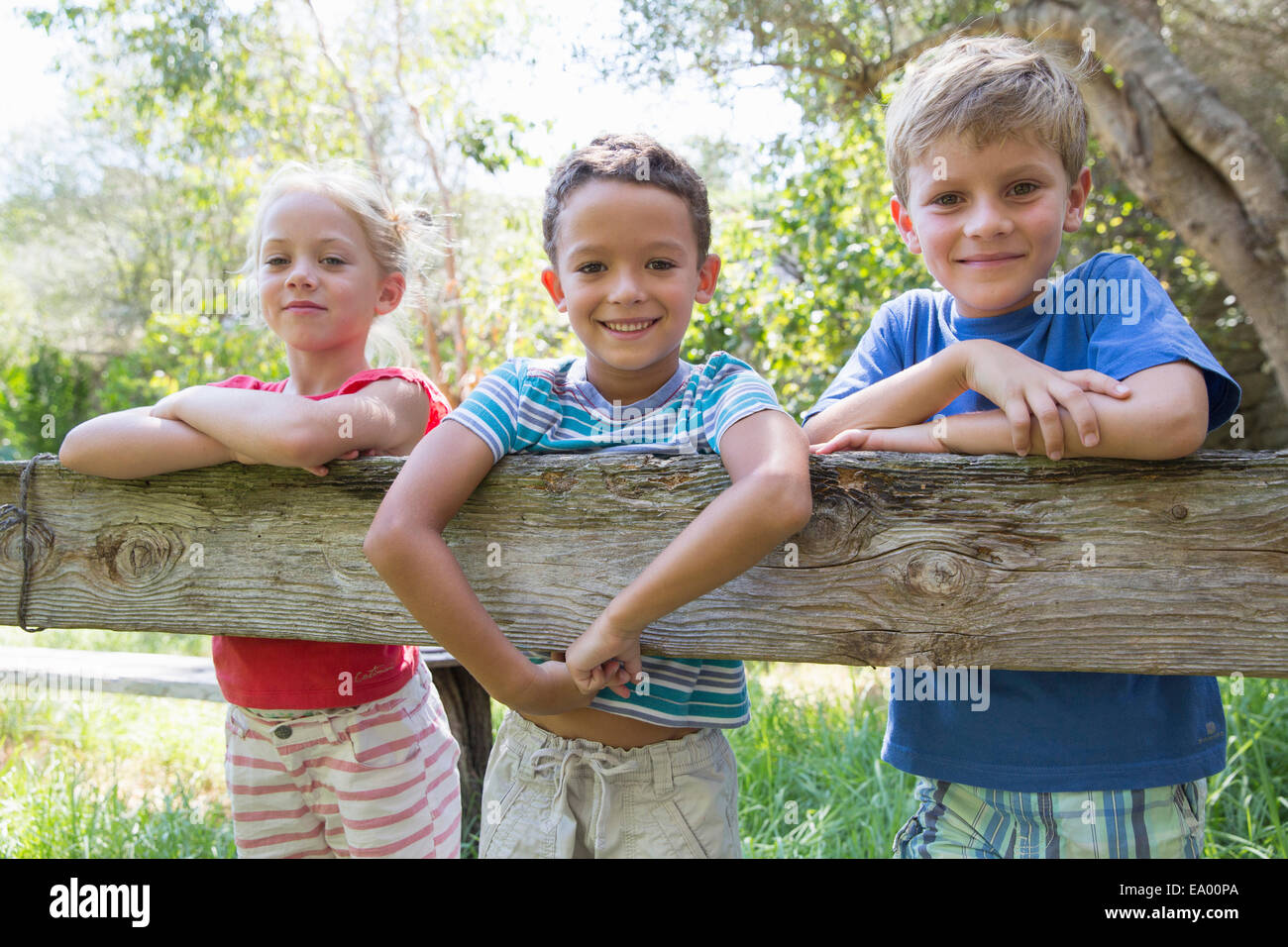 Trois enfants en s'appuyant sur une clôture de jardin Banque D'Images