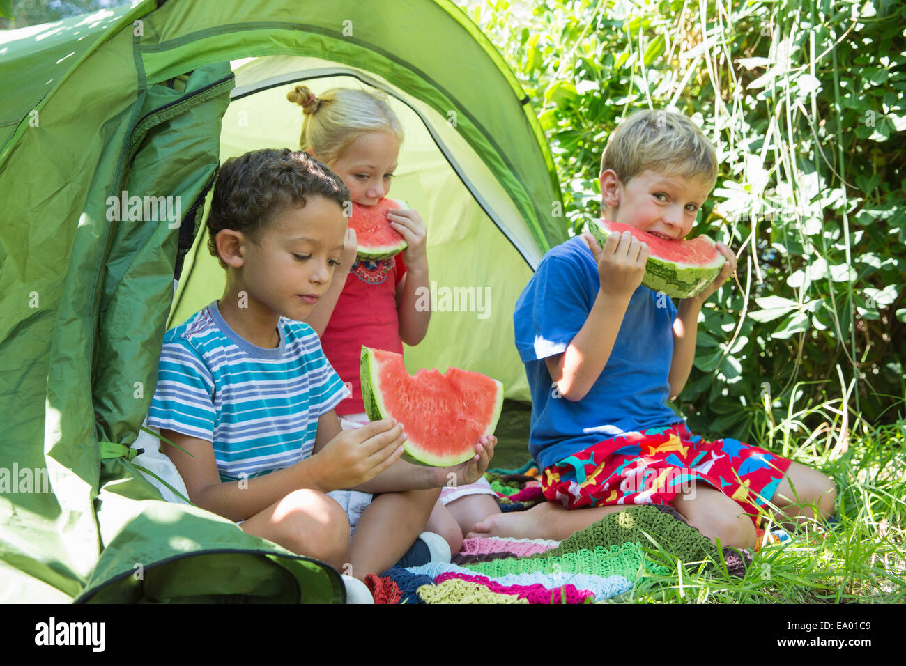 Trois enfants eating watermelon slices dans tente de jardin Banque D'Images