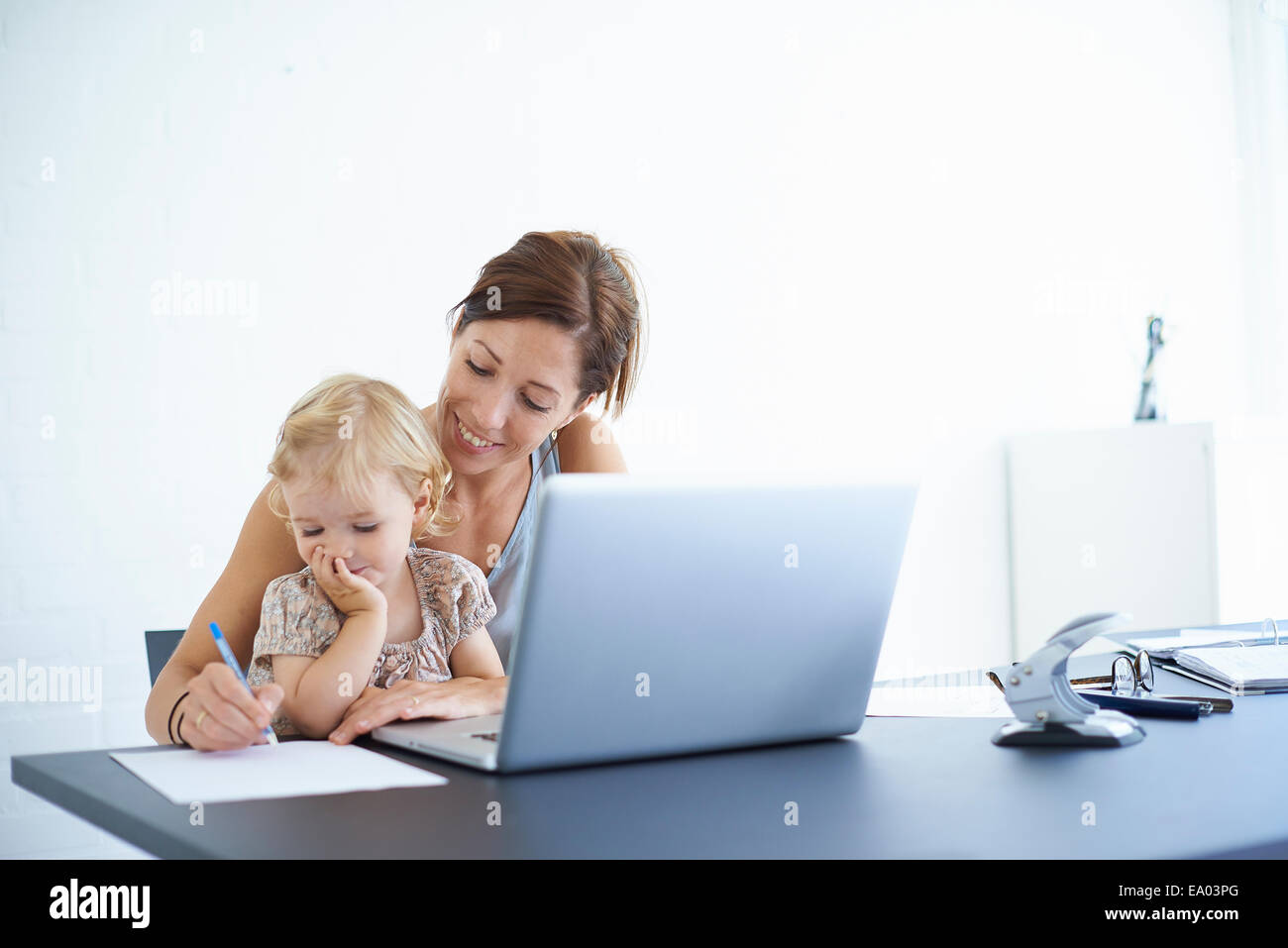 Mid adult woman writing notes avec toddler fille sur ses genoux Banque D'Images