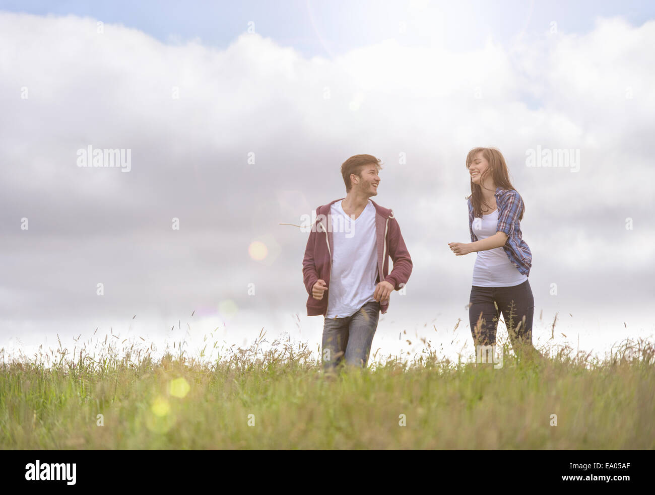 Jeune couple qui traverse la prairie sous un soleil brillant Banque D'Images