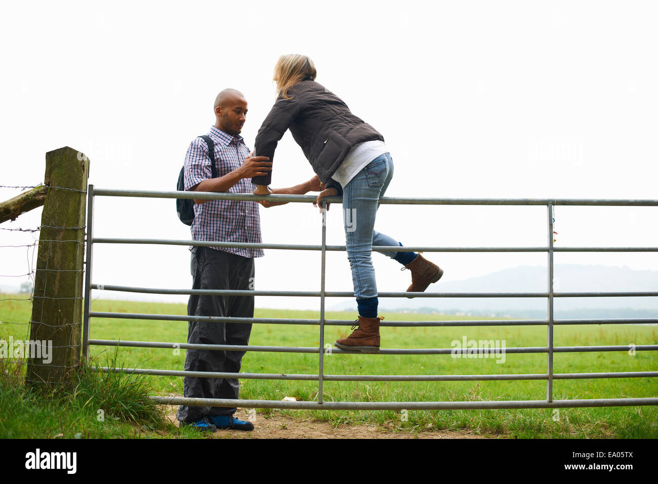 Couple climbing sur gate dans les champs Banque D'Images