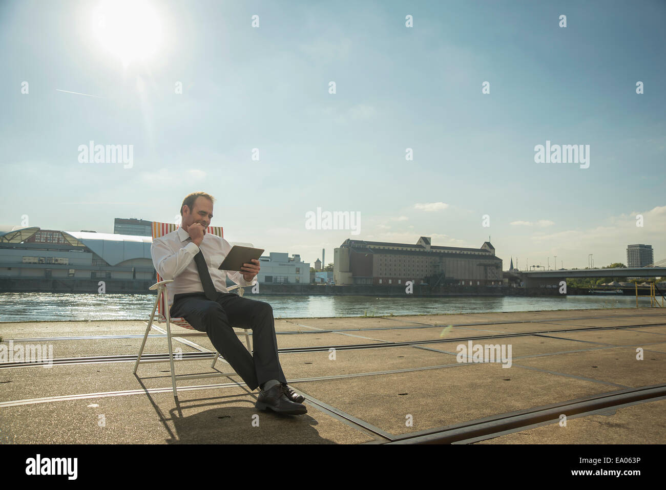 Businessman sitting on chair sur les voies de tram à l'aide de tablet Banque D'Images