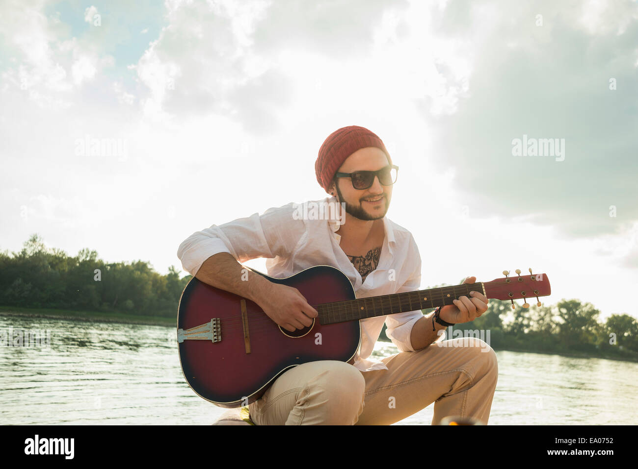 Jeune homme assis au bord du lac à jouer de la guitare Banque D'Images