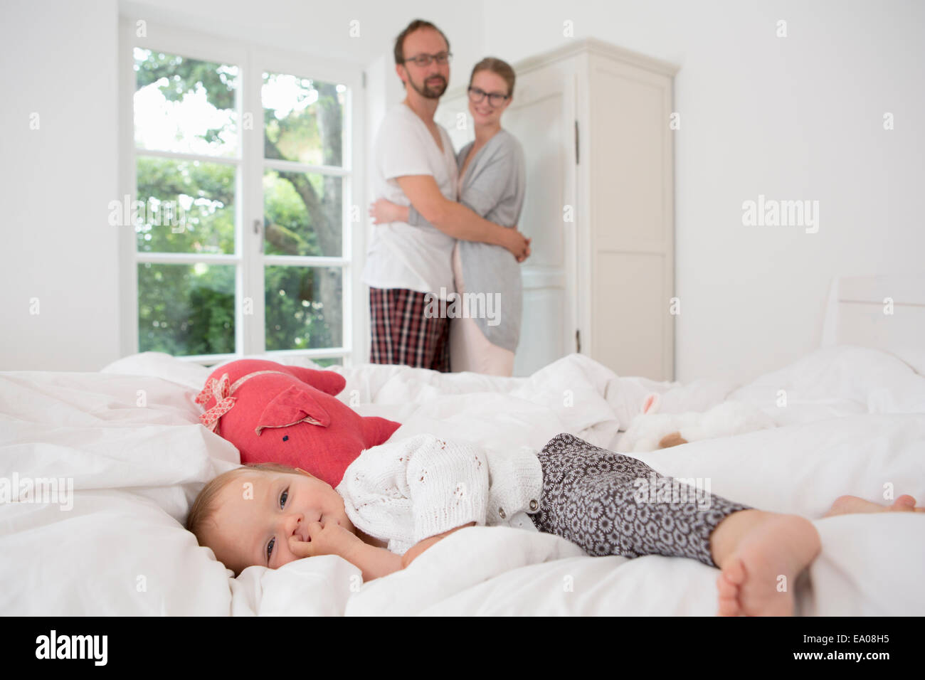 Baby Girl lying on bed, parents en arrière-plan Banque D'Images