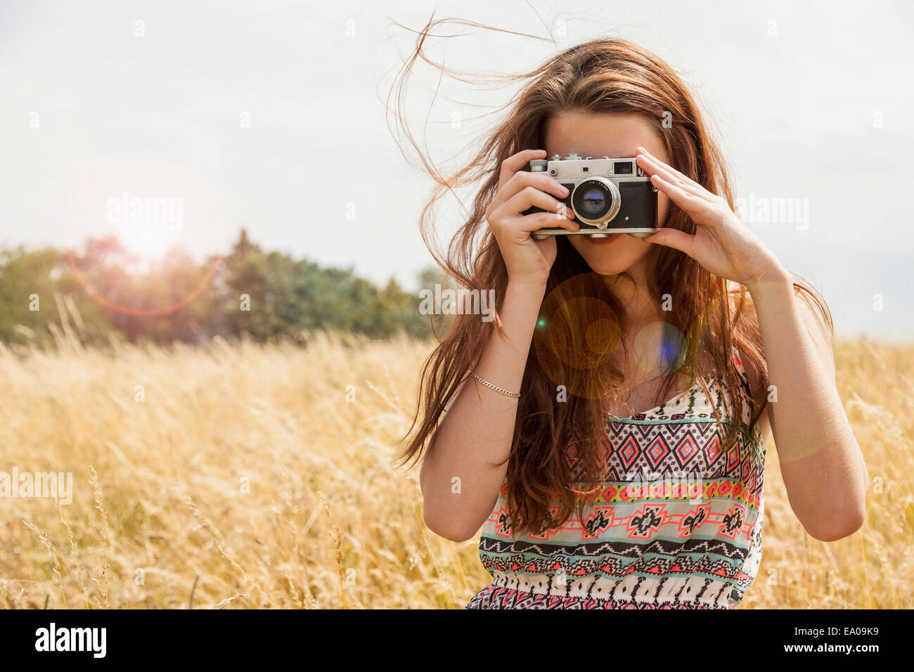 Young woman taking photo with vintage camera in field Banque D'Images