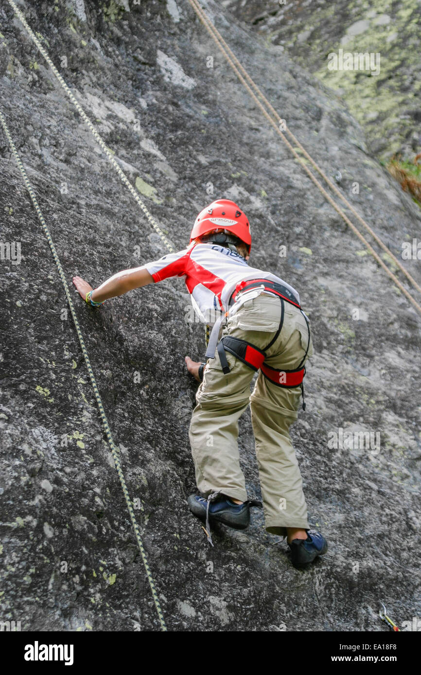 Garçon enfant escalade un rocher dans l'équipement complet Banque D'Images