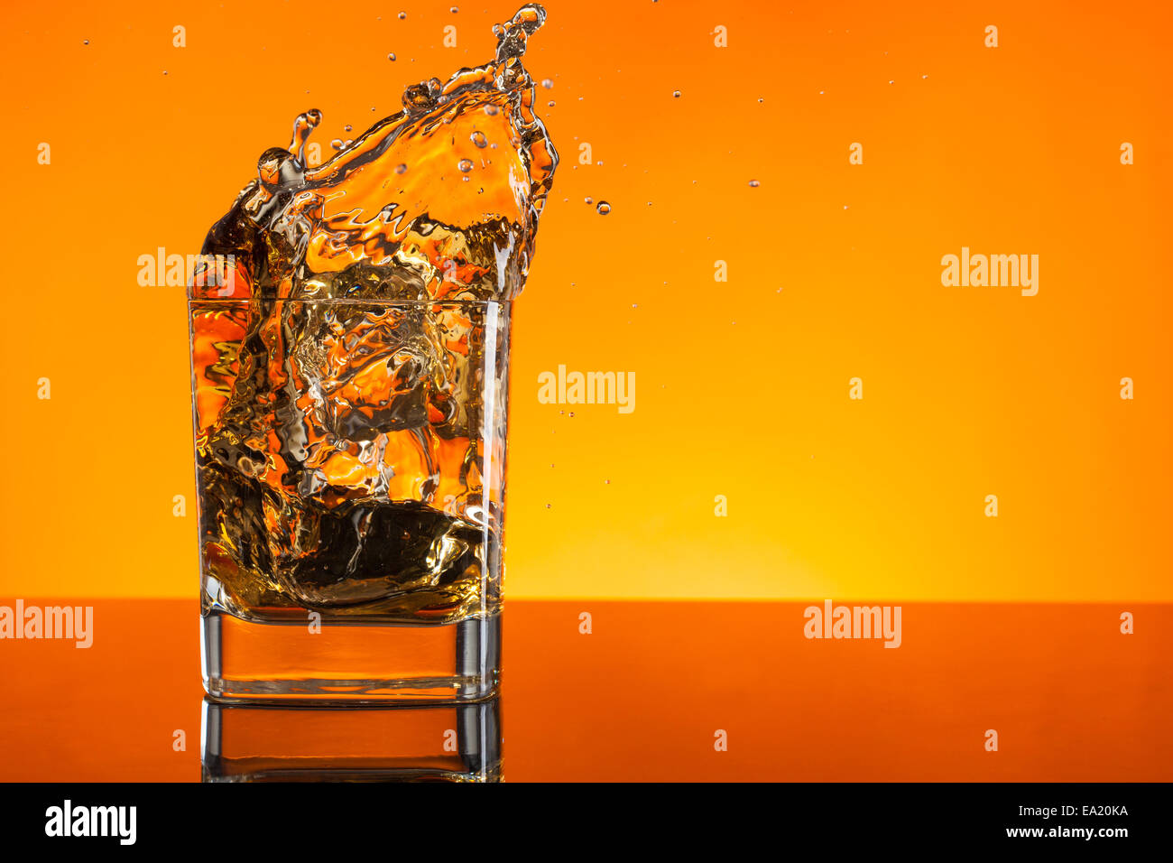Whiskey shot projection de verre sur fond orange Banque D'Images