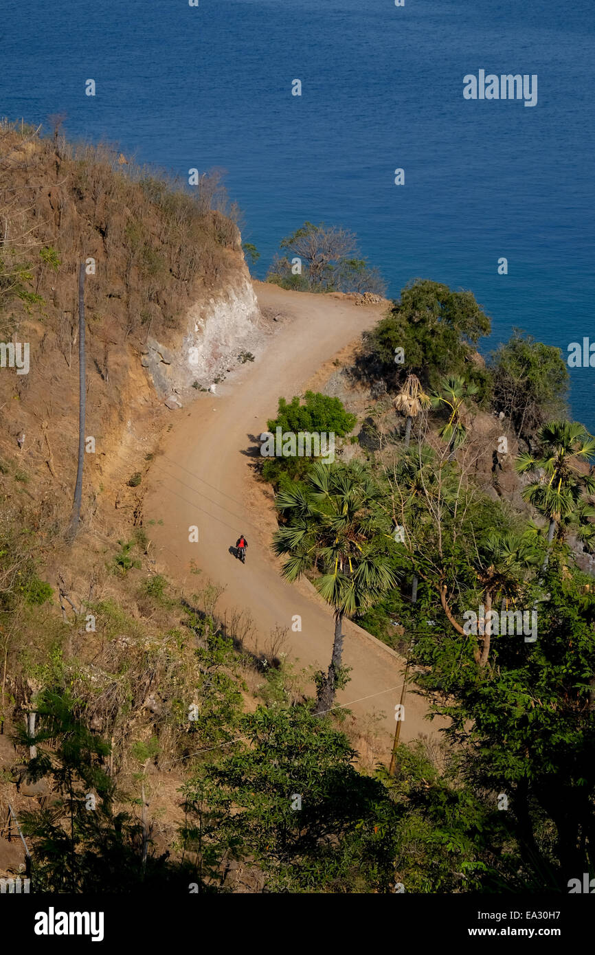 Une route rurale côtière et un automobiliste itinérant sont vus d'une colline côtière à Lamagute, Ile APE Timur, Lembata, Nusa Tenggara est, Indonésie. Banque D'Images