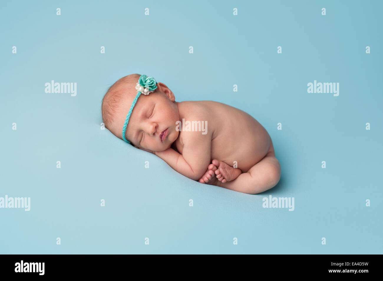 Portrait d'un nouveau-né âgé de sept jours fille de bébé. Elle porte un bandeau de papier rose et perle et dort sur tricot bleu clair Banque D'Images