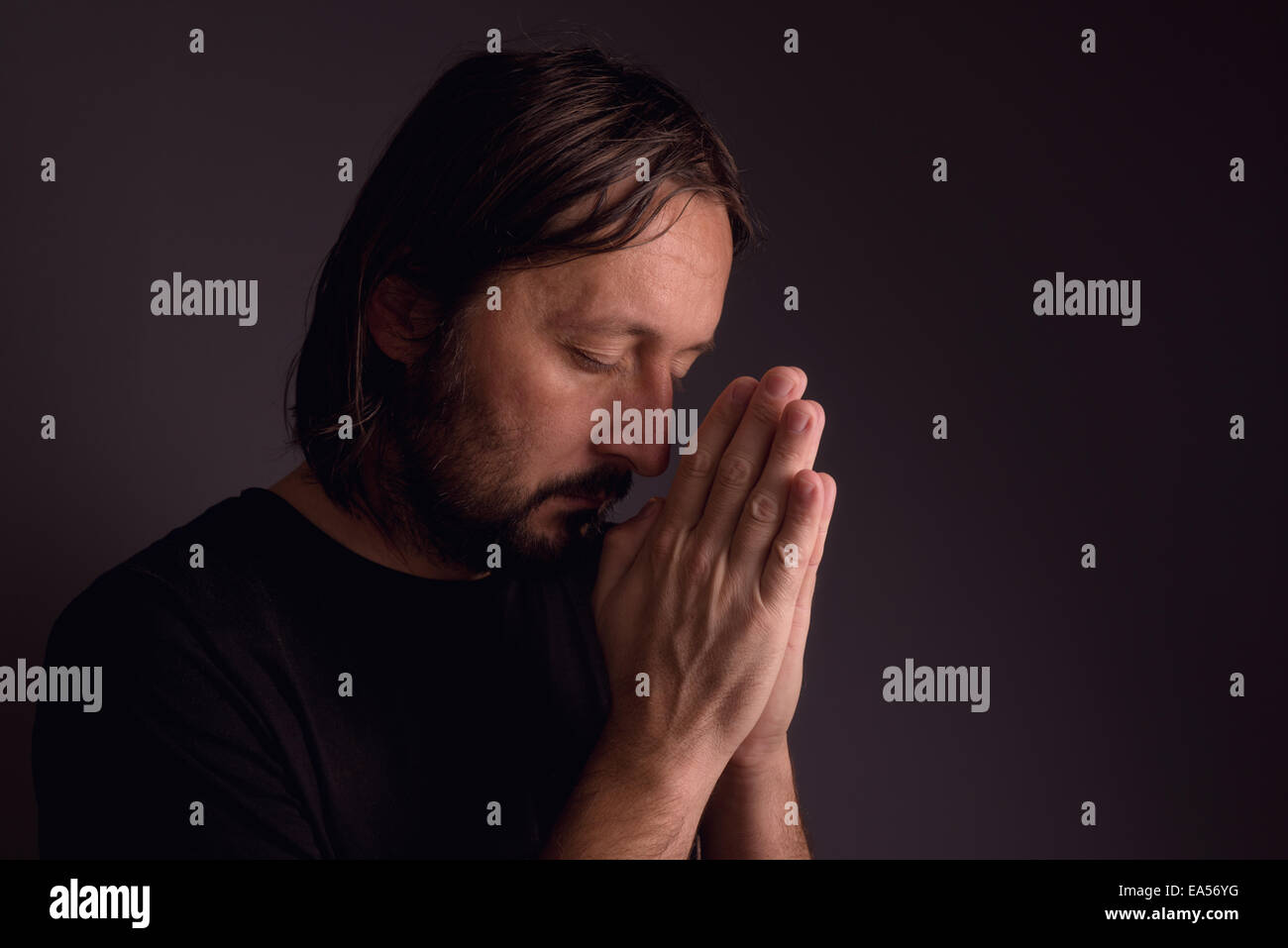 Homme barbu adultes à prier Dieu dans une pièce sombre, concept religieux. Banque D'Images