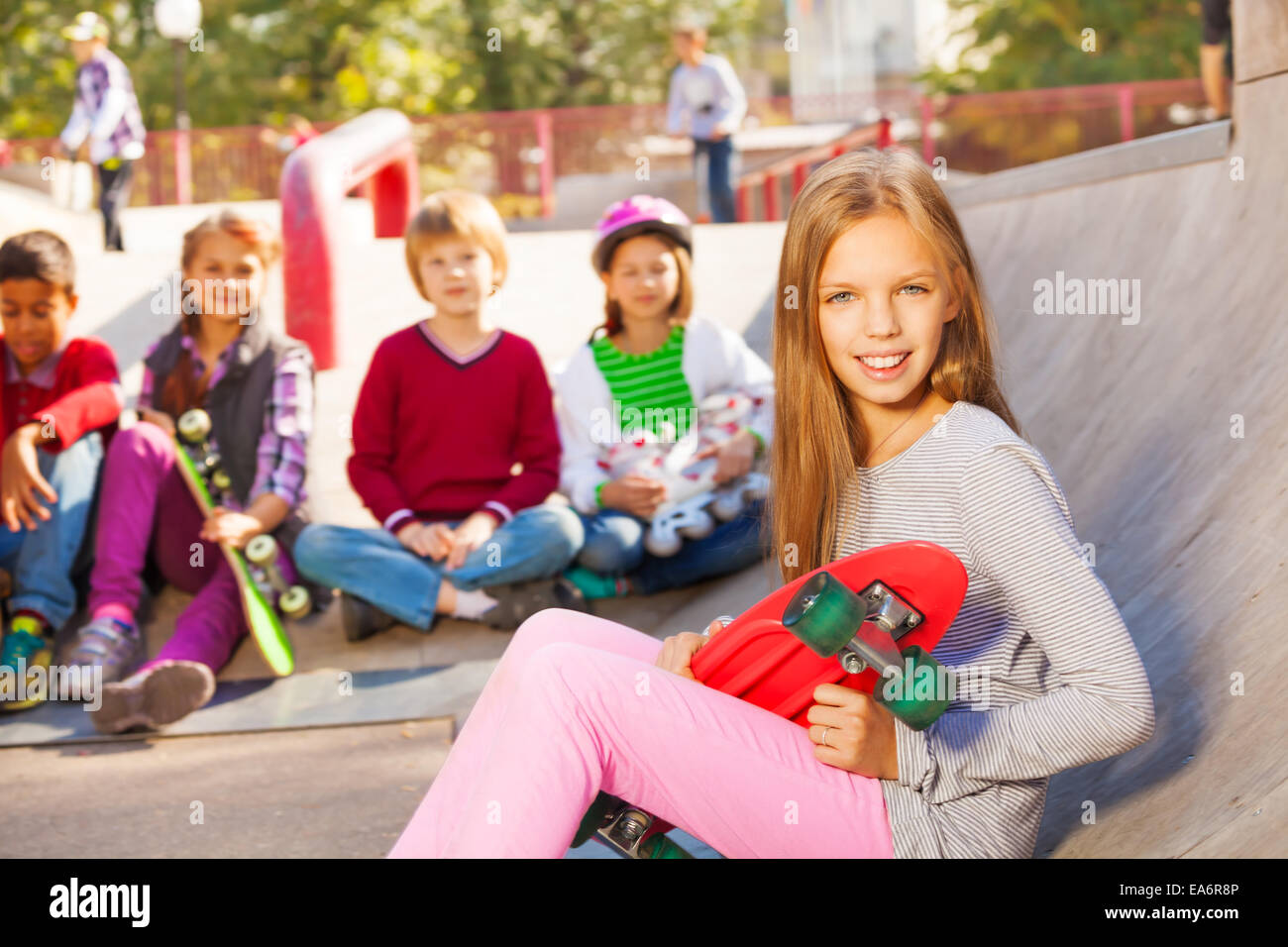 Girl with skateboard et les enfants assis derrière Banque D'Images