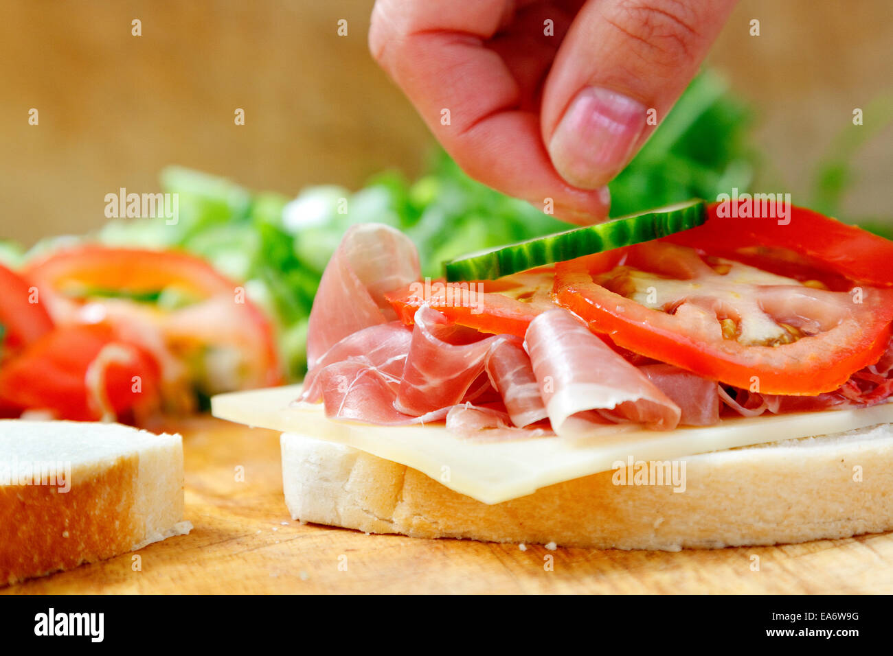 Placer délicatement les doigts femal tranche de concombre sur bloomer blanc sandwich pain de jambon prosciutto, fromage de gruyère et de tranches de tomate Banque D'Images
