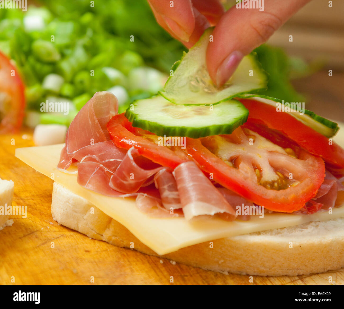 Woman's hand mise sur concombre pain Bloomer blanc sandwich de jambon prosciutto, fromage de gruyère et de tranches de tomate Banque D'Images